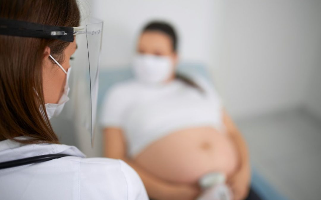 Doctora realizando ultrasonido a una mujer embarazada durante una consulta médica, ambas usando cubrebocas por medidas de protección.