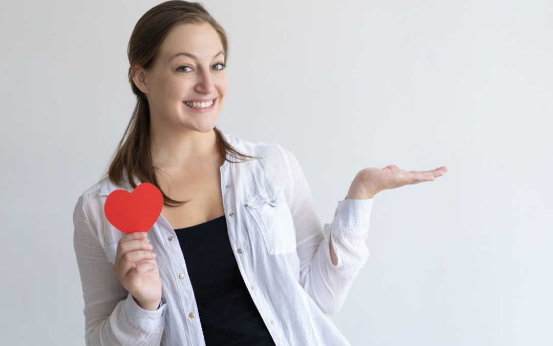 Mujer sonriendo mientras sostiene un corazón rojo, representando la importancia de cuidar la salud cardiovascular.