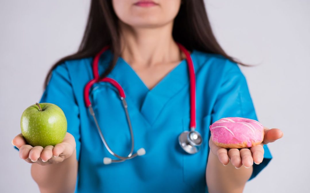 Profesional de la salud sostiene una manzana verde y una dona rosada, simbolizando la elección entre hábitos saludables y riesgos del síndrome metabólico.